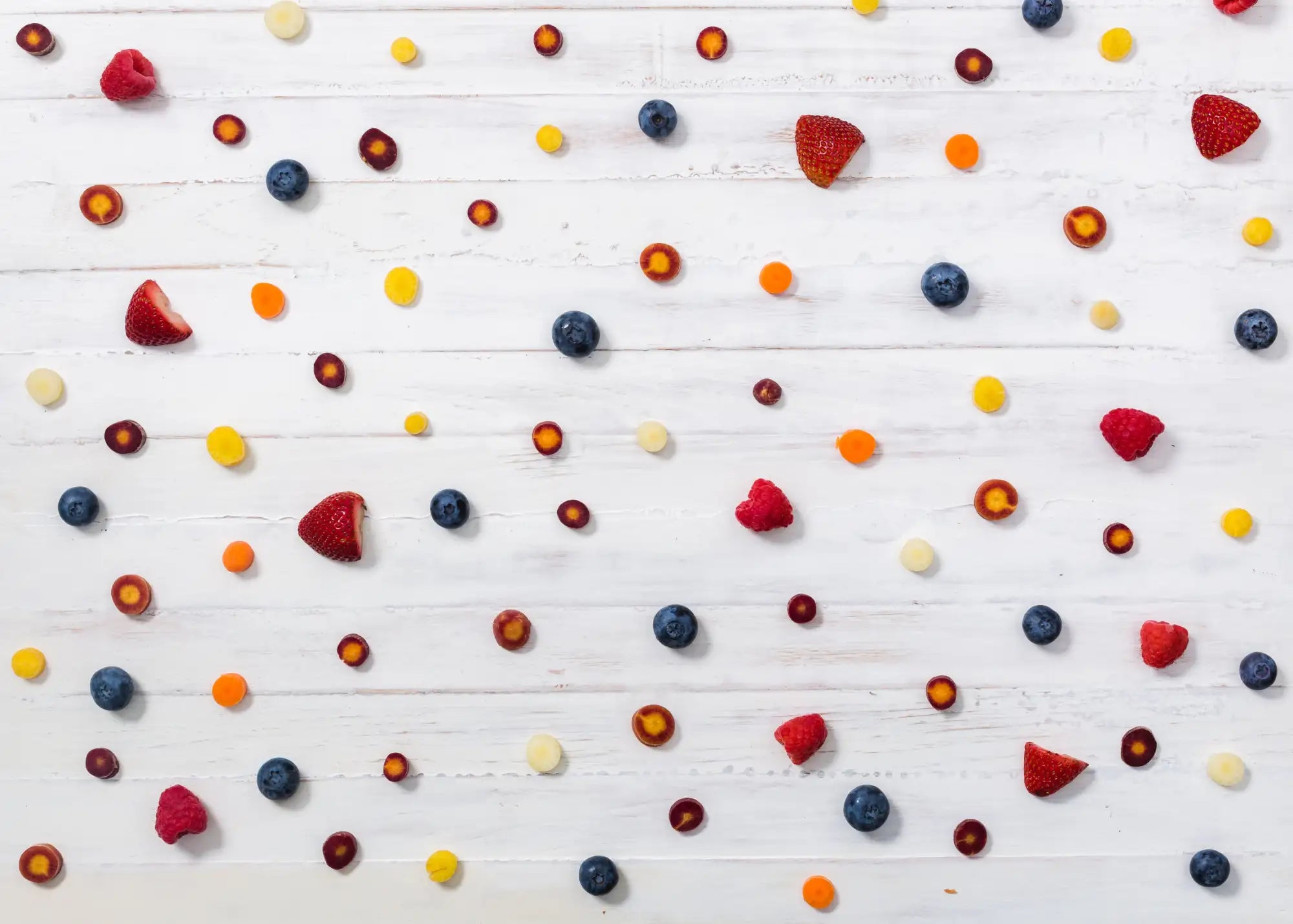 A vibrant assortment of fresh berries and fruit slices scattered across a white wooden surface.